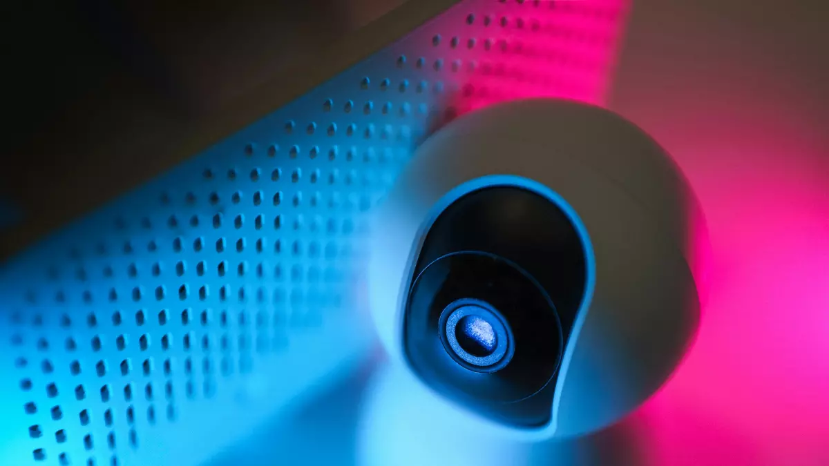 A close-up of a white security camera with a black lens, lit by blue and pink neon lights.